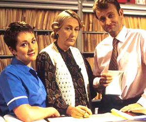 My Hero. Image shows from L to R: Janet Dawkins (Emily Joyce), Mrs Raven (Geraldine McNulty), Dr Piers Crispin (Hugh Dennis). Copyright: Big Bear Films. My Hero. Image shows from L to R: Janet Dawkins (Emily Joyce), Mrs Raven (Geraldine McNulty), Dr Piers Crispin (Hugh Dennis). Copyright: Big Bear Films.
