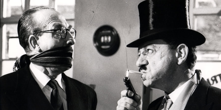 The Big Job. Image shows from L to R: Bank Cashier (Frank Forsyth), George 'The Great Brain' (Sid James). Copyright: Anglo Amalgamated. The Big Job. Image shows from L to R: Bank Cashier (Frank Forsyth), George 'The Great Brain' (Sid James). Copyright: Anglo Amalgamated.
