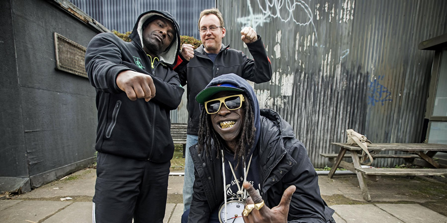 Urban Myths: Public Enemy (feat. Kev Wells). Image shows from L to R: Chuck D (Paterson Joseph), Kev Wells (Philip Glenister), Flavor Flav (Abdul Salis). Urban Myths: Public Enemy (feat. Kev Wells). Image shows from L to R: Chuck D (Paterson Joseph), Kev Wells (Philip Glenister), Flavor Flav (Abdul Salis).