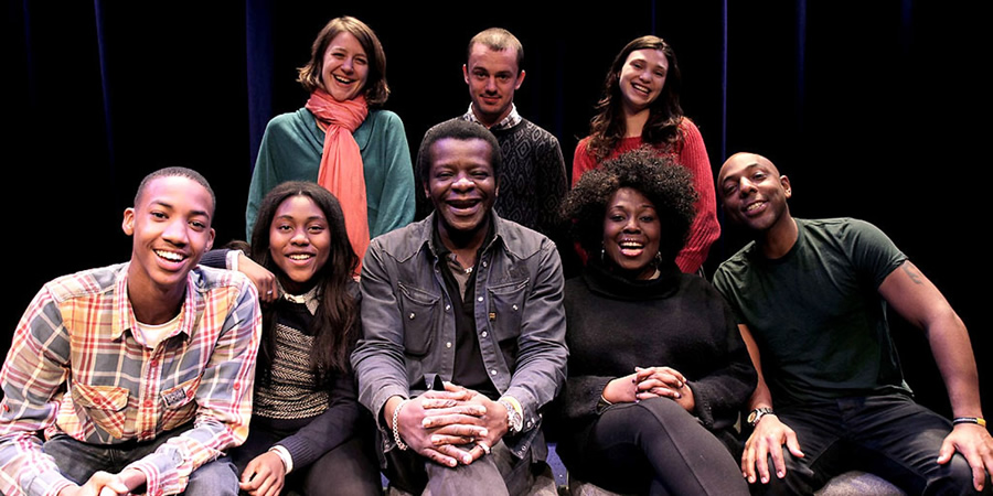 What Does The K Stand For?. Image shows from L to R: Young Stephen (Shaquille Ali-Yebuah), Stephanie Amos (Fatou Sohna), Miss Collins (Gemma Whelan), Stephen K Amos, PE Teacher (Harry Jardine), Fanni (Emerald O'Hanrahan), Virginia Amos (Ellen Thomas), Vincent Amos (Don Gilet). Copyright: BBC. What Does The K Stand For?. Image shows from L to R: Young Stephen (Shaquille Ali-Yebuah), Stephanie Amos (Fatou Sohna), Miss Collins (Gemma Whelan), Stephen K Amos, PE Teacher (Harry Jardine), Fanni (Emerald O'Hanrahan), Virginia Amos (Ellen Thomas), Vincent Amos (Don Gilet). Copyright: BBC.