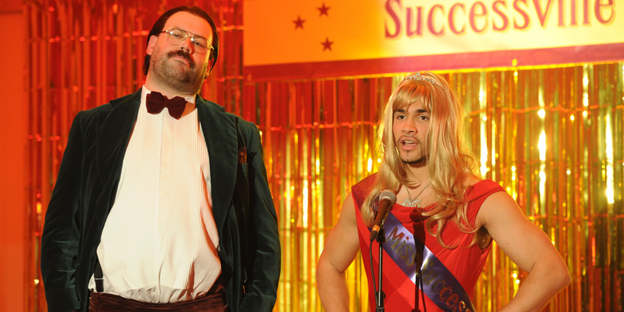 Murder In Successville. Image shows from L to R: DI Sleet (Tom Davis), Louis Smith. Copyright: Tiger Aspect Productions. Murder In Successville. Image shows from L to R: DI Sleet (Tom Davis), Louis Smith. Copyright: Tiger Aspect Productions.