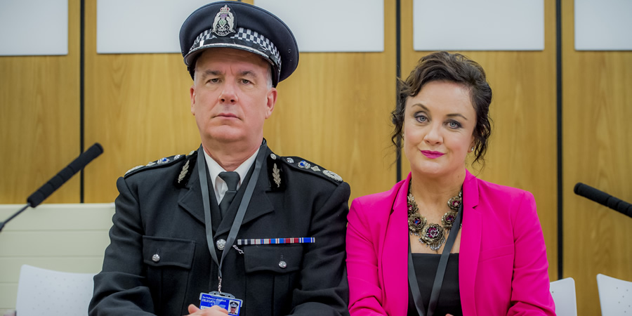Scot Squad. Image shows from L to R: Chief Commissioner Cameron Miekelson (Jack Docherty), Barbara Edwards (Lorraine McIntosh). Copyright: The Comedy Unit. Scot Squad. Image shows from L to R: Chief Commissioner Cameron Miekelson (Jack Docherty), Barbara Edwards (Lorraine McIntosh). Copyright: The Comedy Unit.