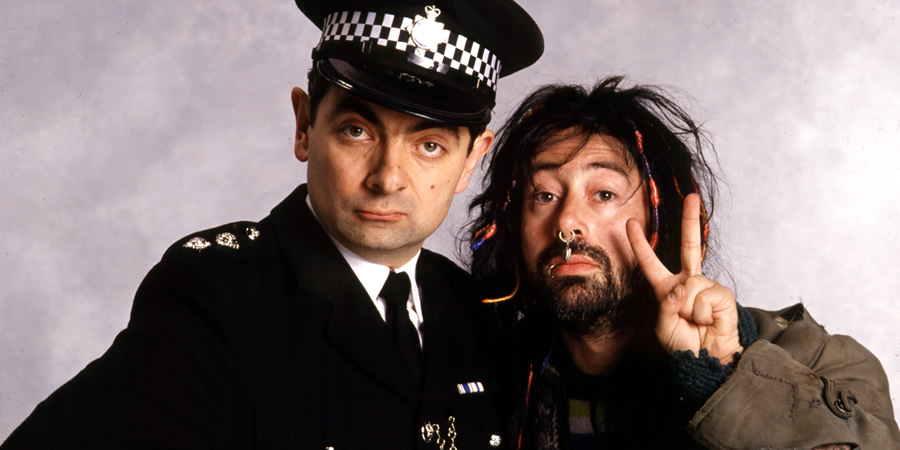The Thin Blue Line. Image shows from L to R: Inspector Fowler (Rowan Atkinson), Traveller Boyfriend (Ben Elton). Copyright: Tiger Aspect Productions. The Thin Blue Line. Image shows from L to R: Inspector Fowler (Rowan Atkinson), Traveller Boyfriend (Ben Elton). Copyright: Tiger Aspect Productions.